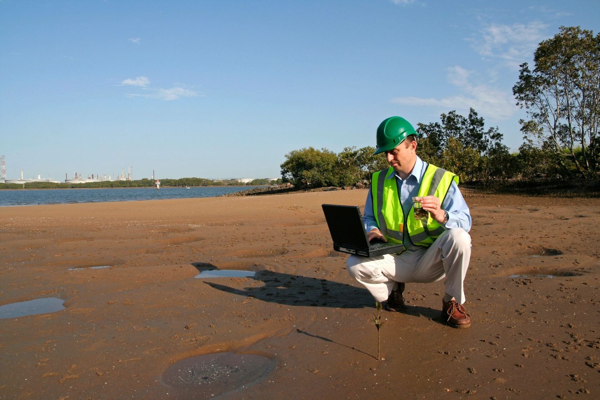 A man kneeling on the beach looking at his laptop.